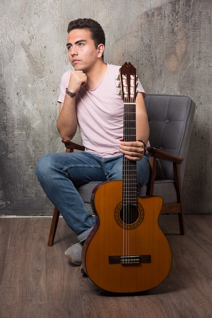 Handsome young man sitting on the chair while holding guitar.