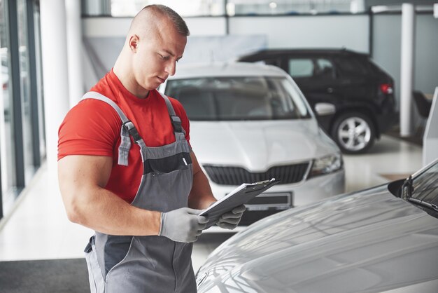 ハンサムな若い男が自動車販売店で話し、ワークショップで車を修理します。