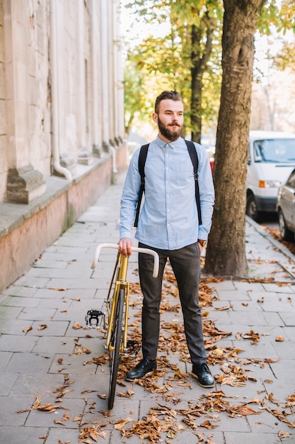 Foto gratuita giovane bello che sta bicicletta vicina