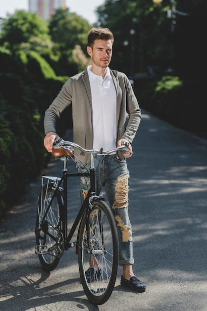 Foto gratuita giovane bello che si leva in piedi con la bicicletta sulla via