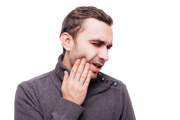 Free photo handsome young man suffering from toothache, touching his cheek to stop pain against white wall