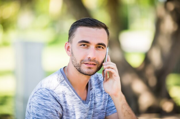 Handsome young man talking on phone while sitting on bench in park