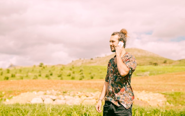 Красивый молодой человек разговаривает по смартфон в сельской местности