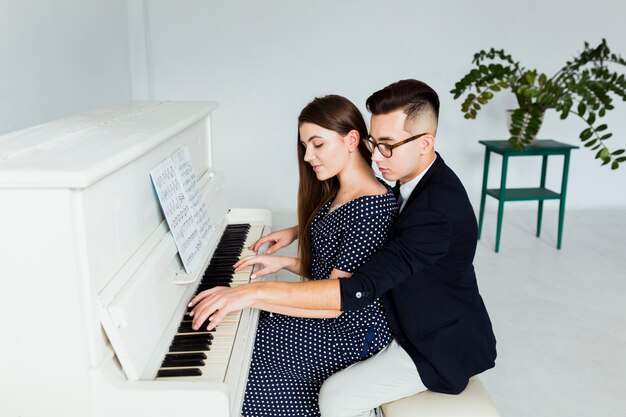 Красивый молодой человек учит свою подругу играть на пианино