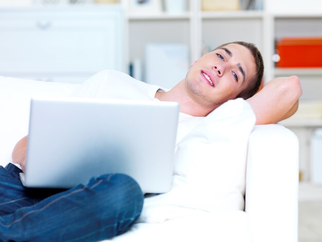 Handsome young man using laptop and lying on the sofa