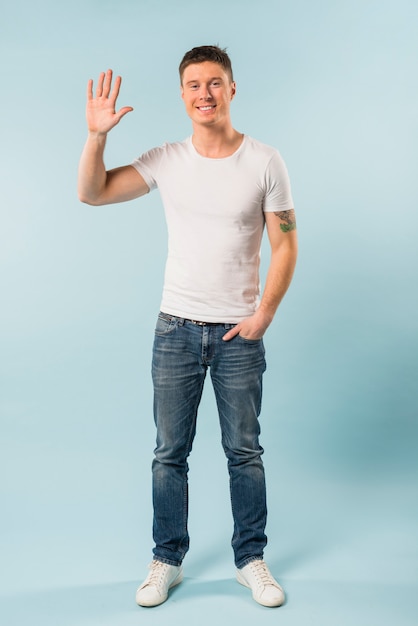 Handsome young man waving her hand against blue backdrop