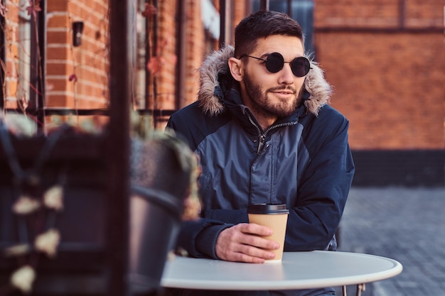 A handsome young man wearing a winter coat sitting with coffee in the outdoor cafe.