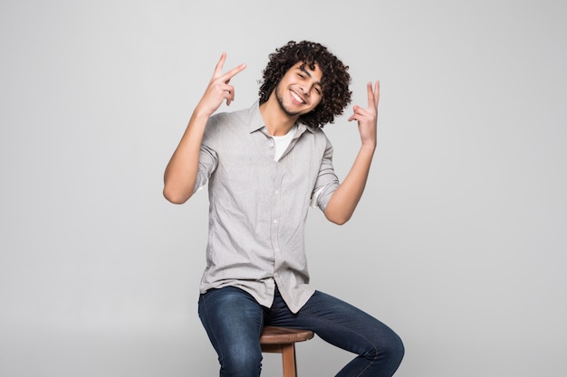 Handsome young man with curly hair sitting on chair over white wall