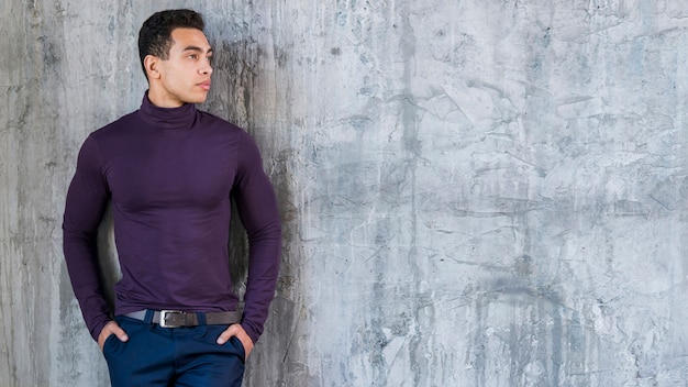 Handsome young man with his hands in pocket leaning against grey wall