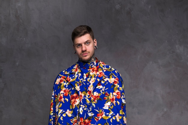 Handsome young man with pierced nose and ears wearing floral coat against grey backdrop