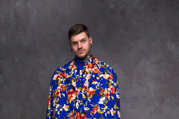 Handsome young man with pierced nose and ears wearing floral coat against grey backdrop