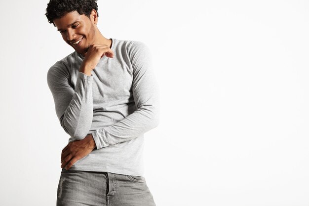 Handsome young model laughing quietly with arms in front of torso, wearing gray cotton longsleeve t-shirt and gray jeans