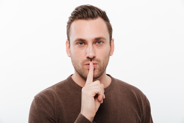 Handsome young serious man showing silence gesture