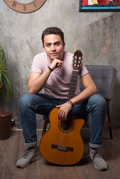 Handsome young sitting on the chair and holding a guitar.