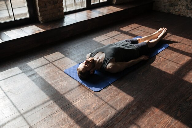 Handsome young strong sportsman in gym lies on floor