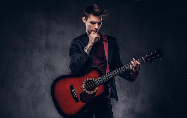 Бесплатное фото Красивый молодой вдумчивый музыкант со стильными волосами в элегантной одежде позирует с гитарой в руках. изолированные на темном фоне.