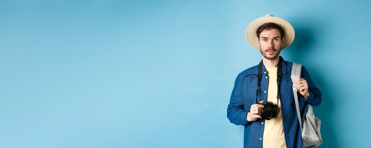 Free Photo handsome young tourist in summer hat backpacking and travelling holding photo camera standing on blu