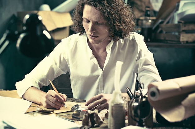 Handsome young writer sitting at the table and writing something in his sketchpad at home