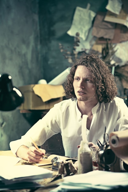 Handsome young writer sitting at the table and writing something in his sketchpad at home