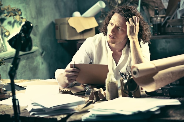 Handsome young writer sitting at the table and writing something in his sketchpad at home