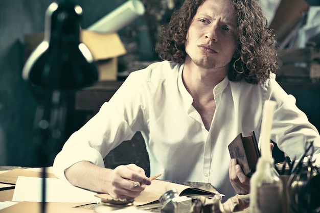 Handsome young writer sitting at the table and writing something in his sketchpad at home