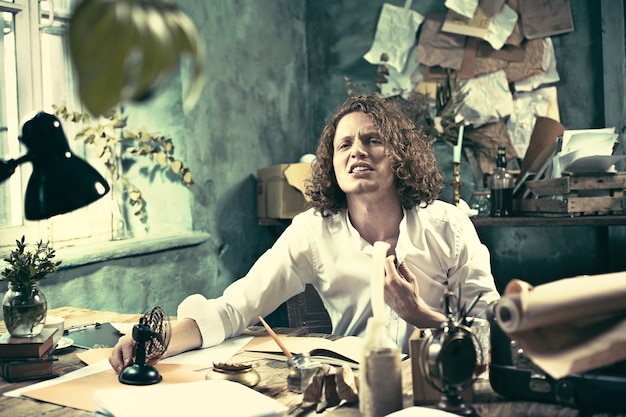 Handsome young writer sitting at the table and writing something in his sketchpad at home