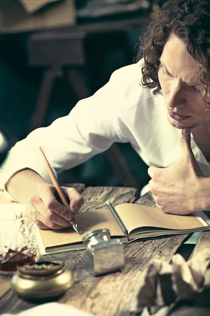 Handsome young writer sitting at the table and writing something in his sketchpad at home