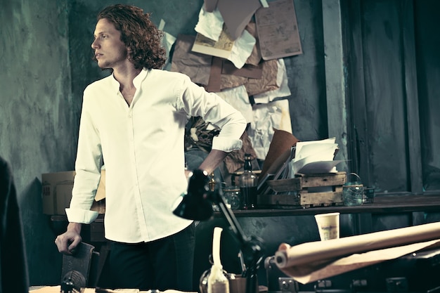 Handsome young writer standing near the table and making up something in his mind at home