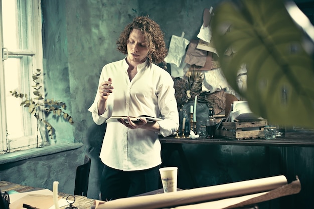 Free photo handsome young writer standing near the table and making up something in his mind at home