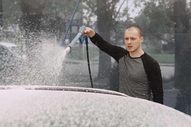 Uomo di handsomen in un maglione nero che lava la sua automobile