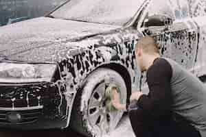 Foto gratuita uomo di handsomen in un maglione nero che lava la sua automobile