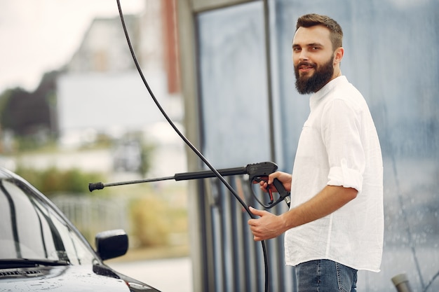 Uomo di handsomen in una camicia bianca che lava la sua automobile