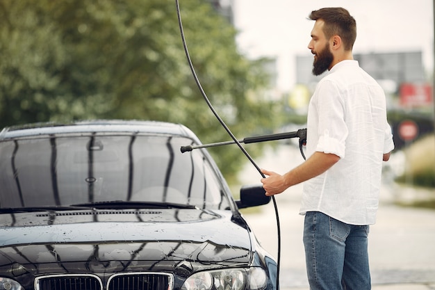 Handsomen man in a white shirt washing his car 