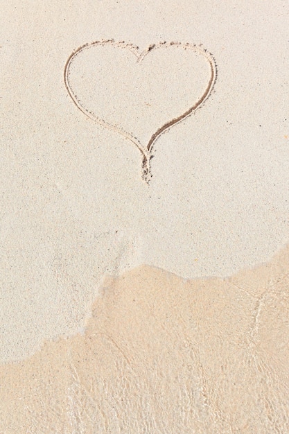 Handwritten heart in sand with wave approaching in the beach