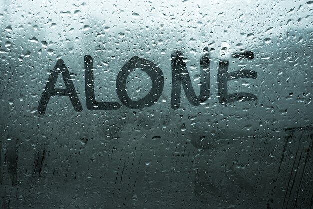 Handwritten word alone on fog up window with rain drops in cold tones