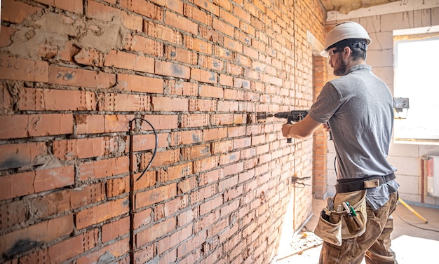 Handyman at a construction site in the process of drilling a wall with a perforator.