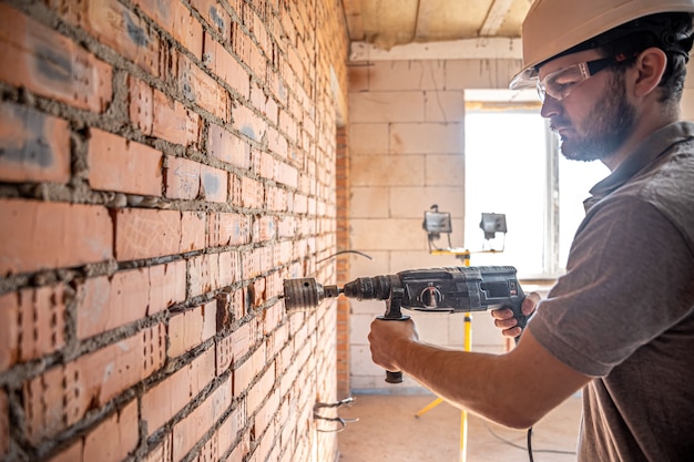 Foto gratuita tuttofare in un cantiere in procinto di perforare un muro con un perforatore