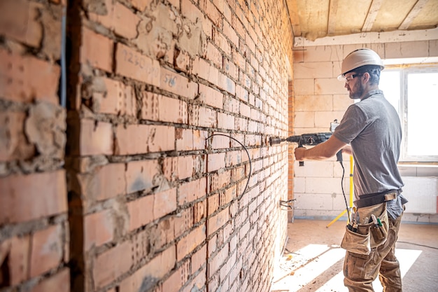 Handyman at a construction site in the process of drilling a wall with a perforator