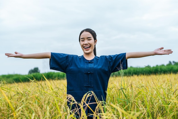 幸いなことに、有機田んぼに立って両手を広げて立っているアジアの若い女性農家