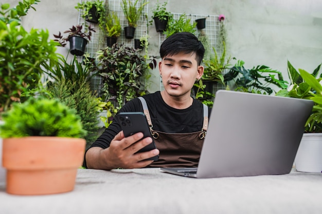 幸いな庭師の男は、店で鉢植えの計画に関するオンラインチュートリアルをしながらスマートフォンとラップトップコンピューターを使用します