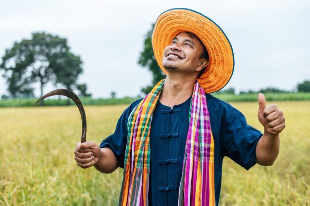 麦わら帽子とふんどしを身に着けて、田んぼに鎌を持って、どろどろと立っている幸せな若い農夫