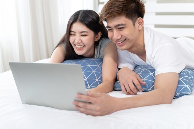 К счастью, молодая красивая женщина и красивый мужчина, используя портативный компьютер на кровати в спальне у себя дома