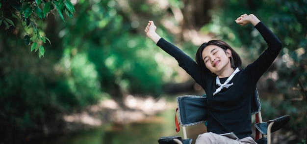 Happily young woman sitting on chair while relax time on camping in forest copy space