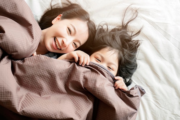행복 아시아 가족 순간 엄마와 딸은 흰색 침대 홈 인테리어 배경에 담요와 함께 놀고 누워