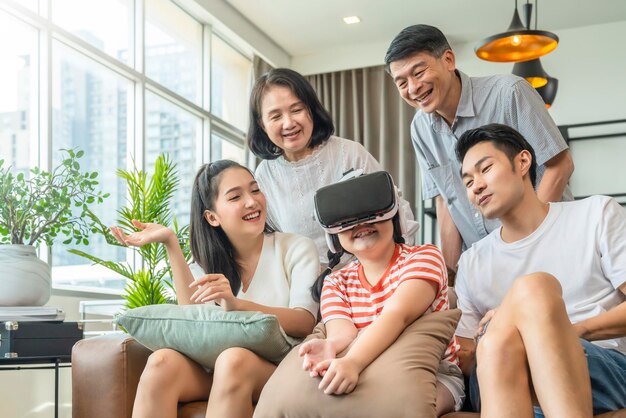 Happiness asian family multi age generation enjoy watch and cheering her daughter up playing vr goggle together with fun and exited in living room home interior background quarantine weekend