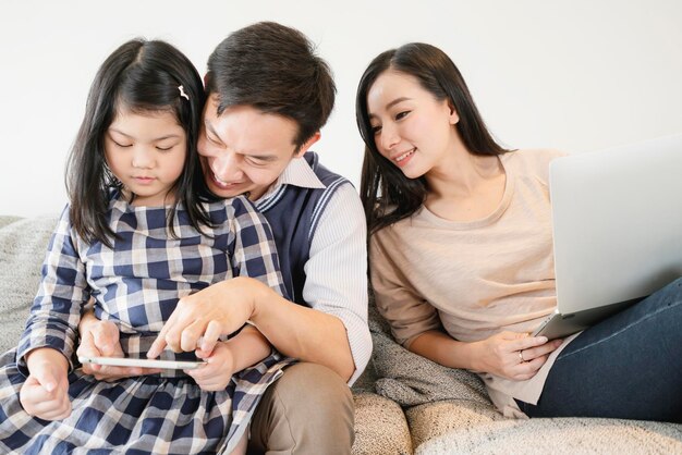 Счастье азиатских семейных каникул на выходных с мамой, папой, дочерью, оставайтесь вместе, используйте планшет и ноутбук, домашний интерьер, фон