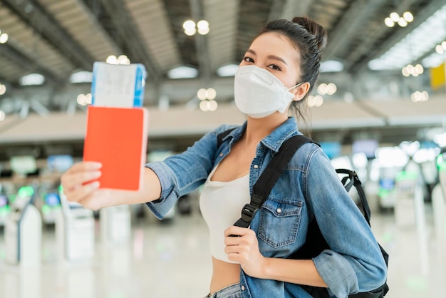 행복 아시아 여성 여행자는 스마트폰 쇼 화면과 여권을 들고 공항 터미널 출발에서 해외로 여행할 준비가 되어 있습니다. covid 잠금이 끝난 후 새로운 일반 생활 방식 여행