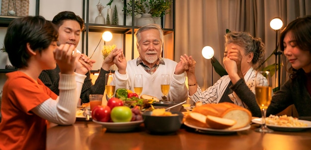 幸福アジアの多世代の食事一緒に家族が手をつないで、休日の夕食の前に感謝祭を祈る祖父母の孫が感謝祭の伝統的な夕食の家に一緒に滞在する