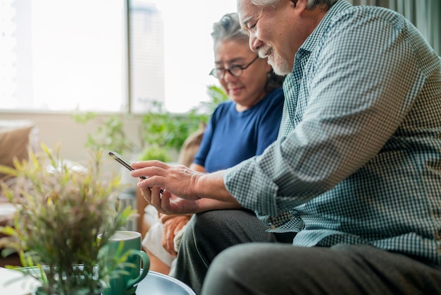 Happiness asian old senior retired couple enjoy videocall to family together on sofa in living room at homeasian people use smartphone communication to family home isolation ides concept