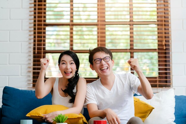 Счастье азиатской сладкой парочки наслаждается телешоу на телевидении вместе в гостиной дома фон